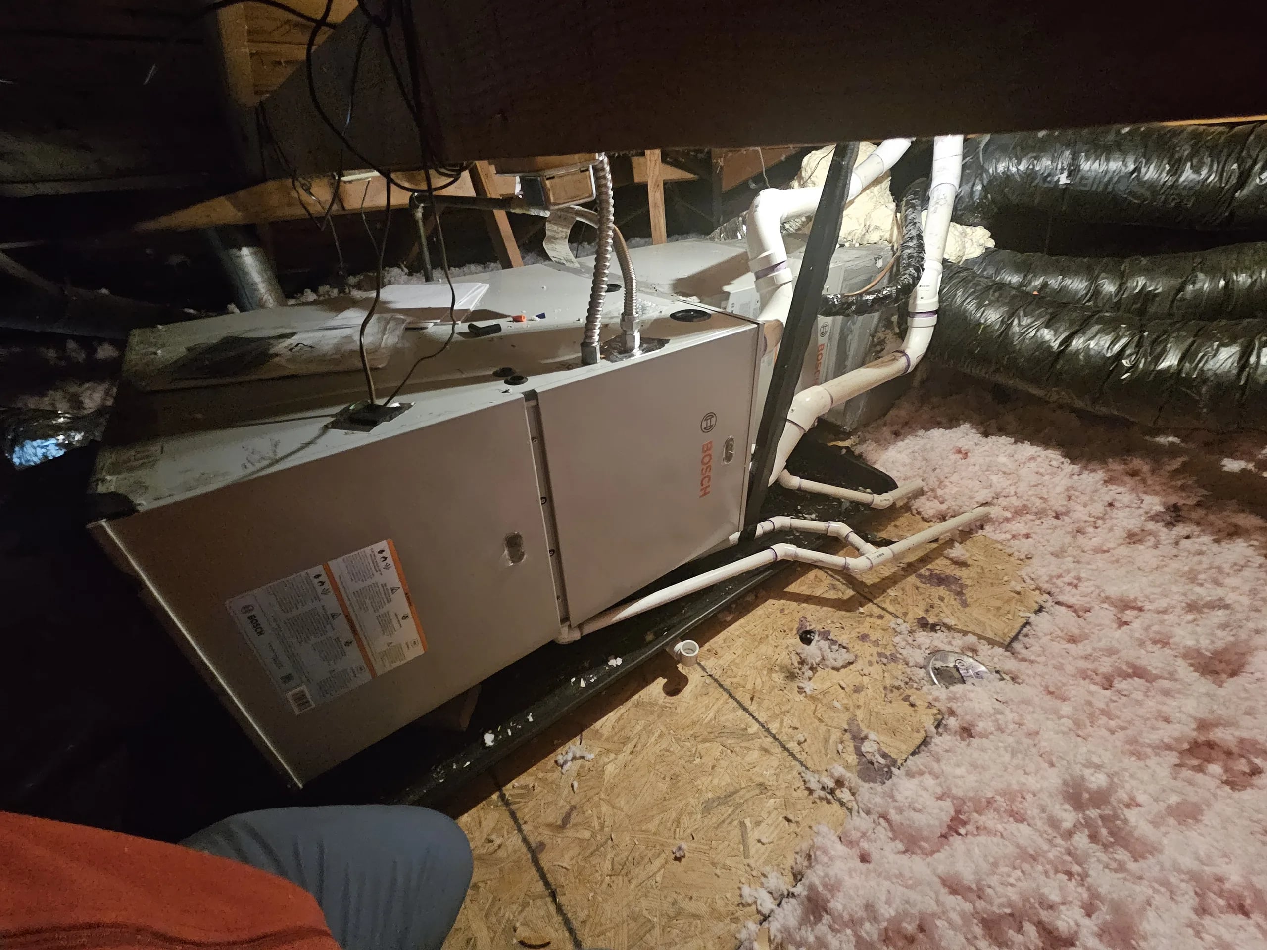 A furnace laid on its side in an attic, with insulated flex ducts over pink insulation