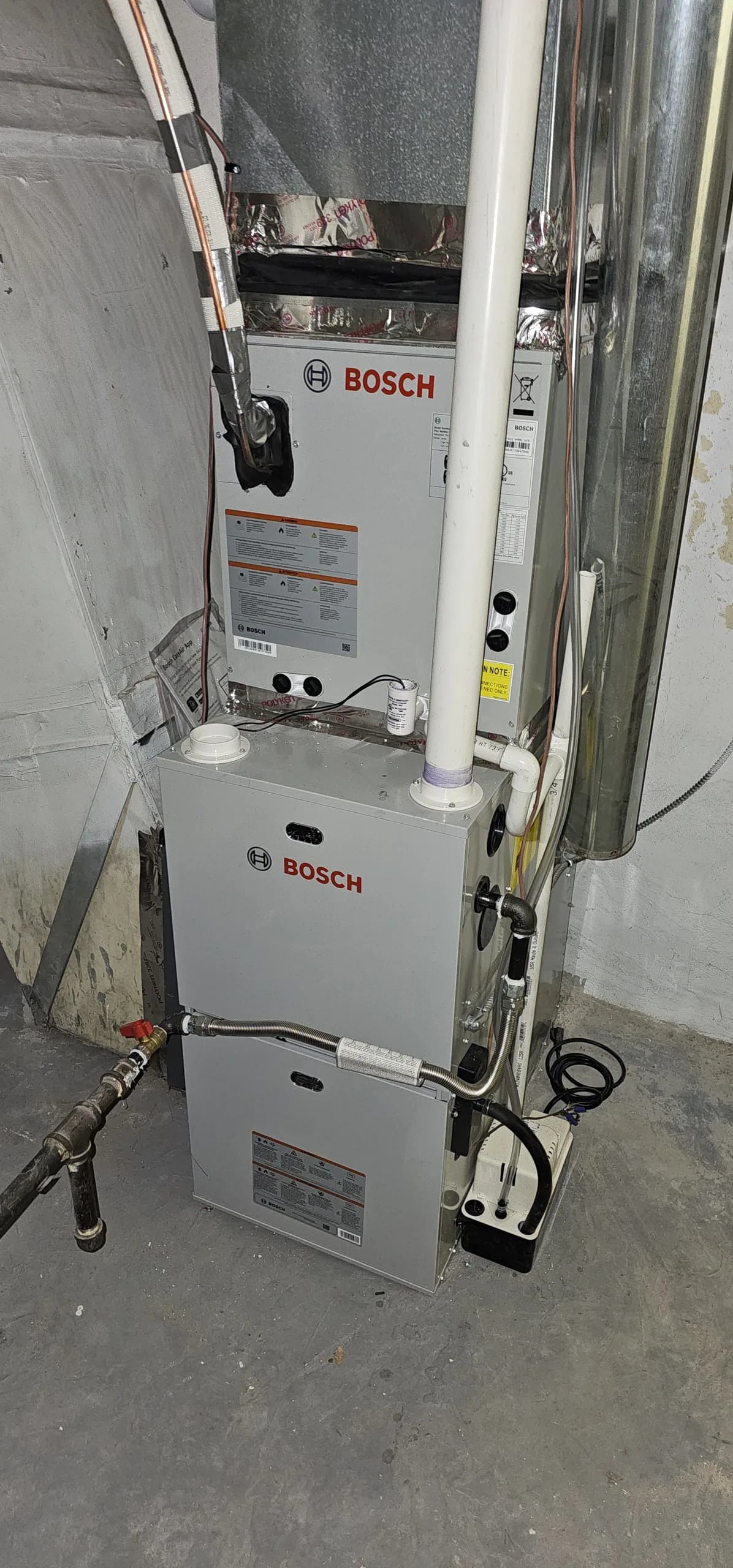 A Bosch furnace and air handler with white PVC venting in a basement utility room