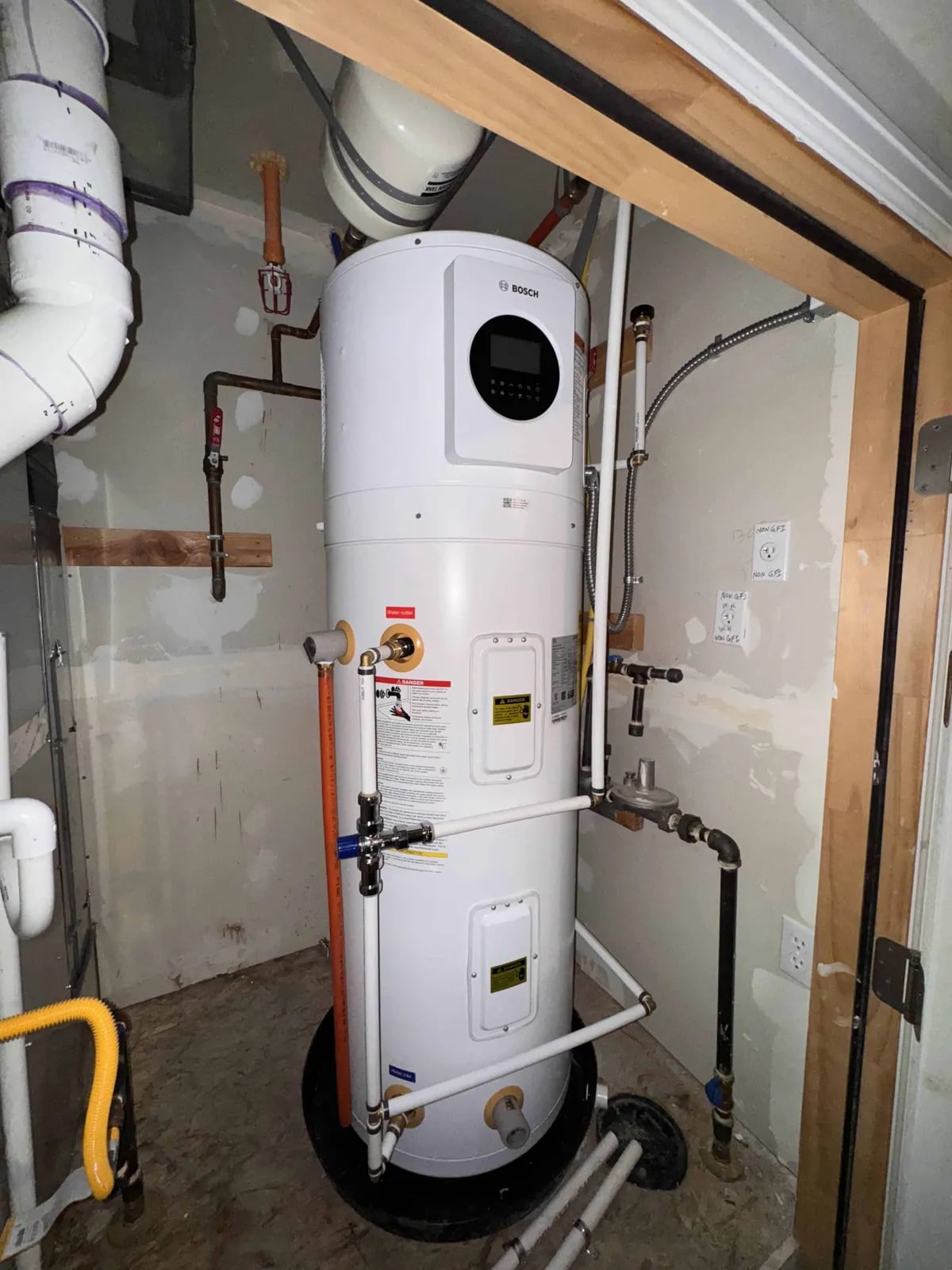 A white Bosch heat pump water heater in a framed utility alcove