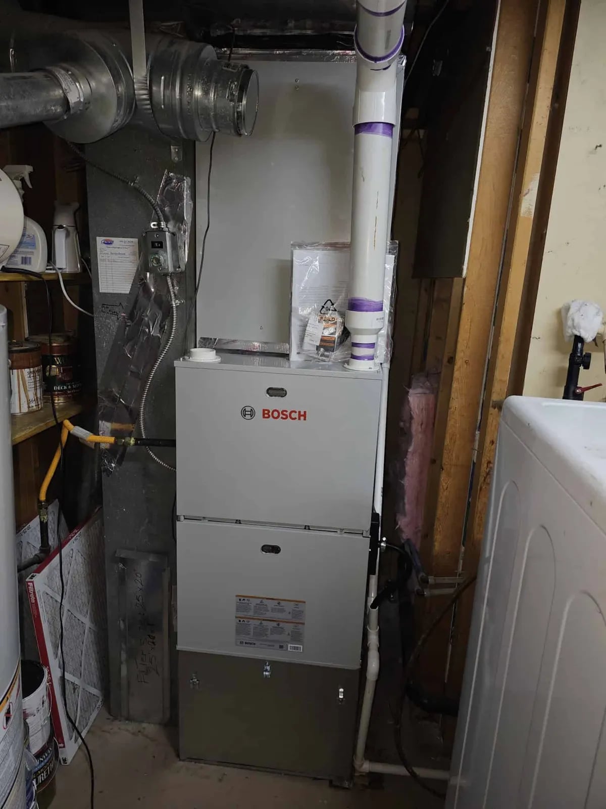 Bosch furnace with purple-taped pipes in a basement utility room by a washer.