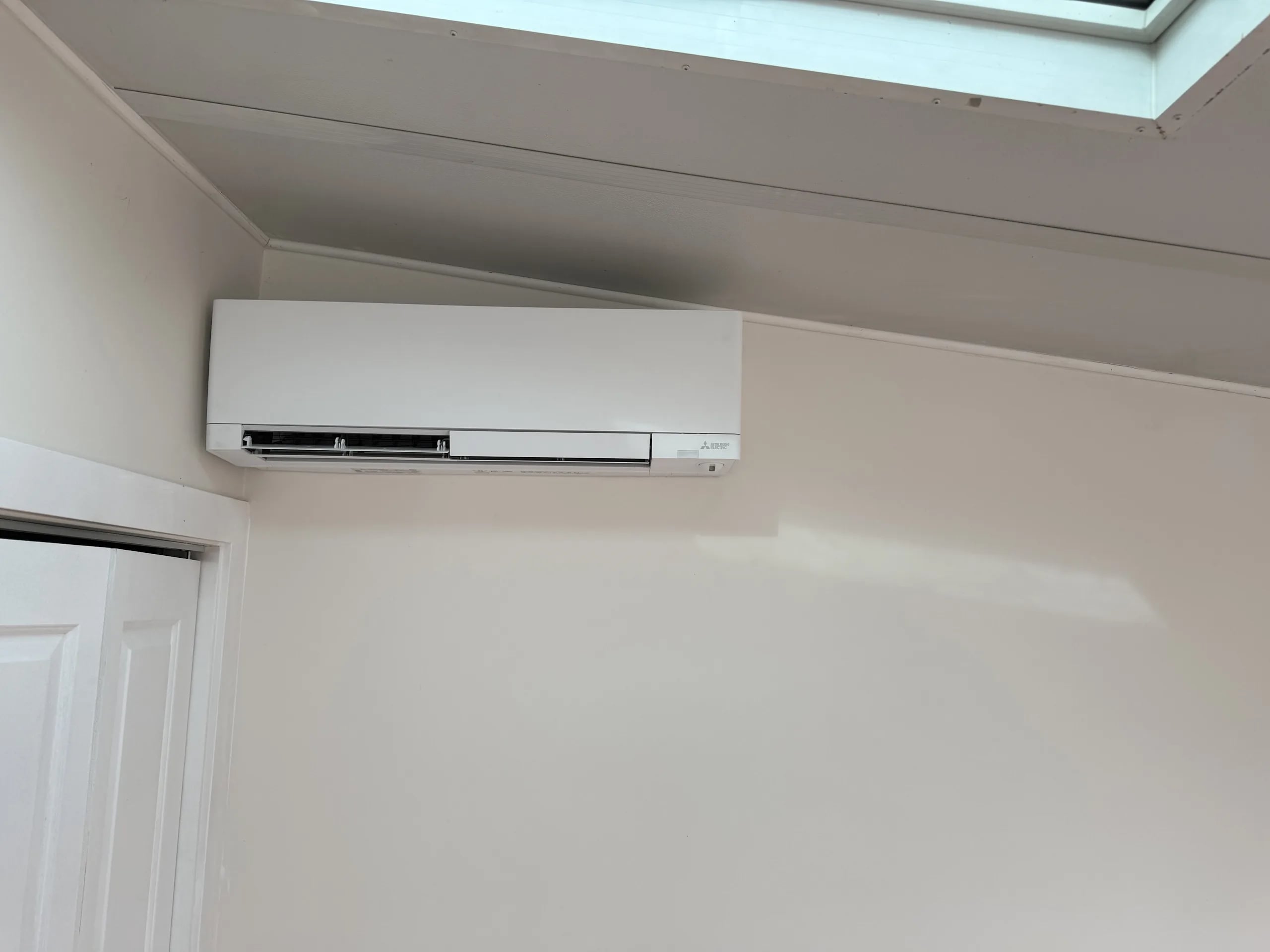 A Mitsubishi wall-mounted head on a white wall below a skylight